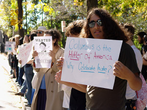 Protest with signs for Indigenous Peoples Day, front sign reads: "Columbus is the Hitler of America. Why Celebrate hate?"